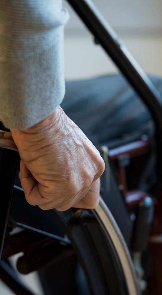 Paralyzed old man using his wheelchair. Closeup of hand of disabled man pushing wheel of wheelchair. Detail of hand of senior man holding the wheel of wheelchair.
